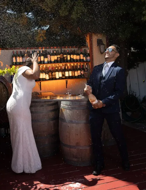 Novios brindando en una boda rústica con barriles de madera y luces cálidas. Fotografía profesional de bodas por David Sánchez.