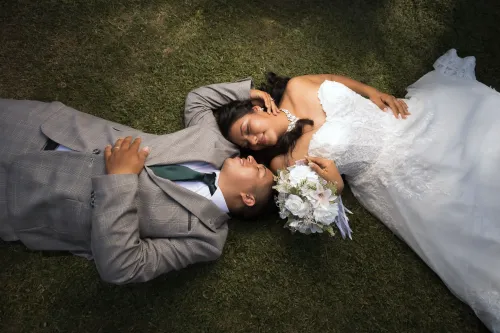 Recién casados acostados en el césped, mirándose con amor. Imagen romántica de boda al aire libre por David Sánchez.