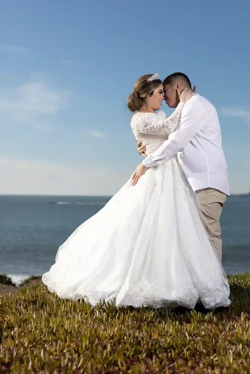 Pareja de recién casados besándose con un fondo de mar y cielo azul. Foto romántica de boda en la playa por David Sánchez.