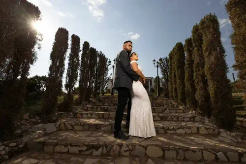 Pareja de novios posando en unas escalinatas rodeadas de cipreses. Sesión de boda en exteriores con toque cinematográfico por David Sánchez.